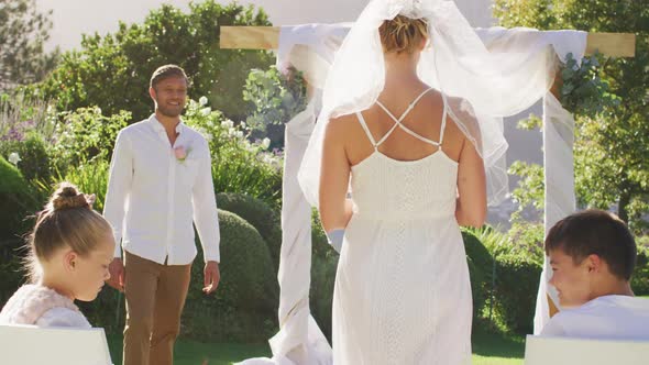 Caucasian bride walking to outdoor altar to groom and wedding officiant alt
