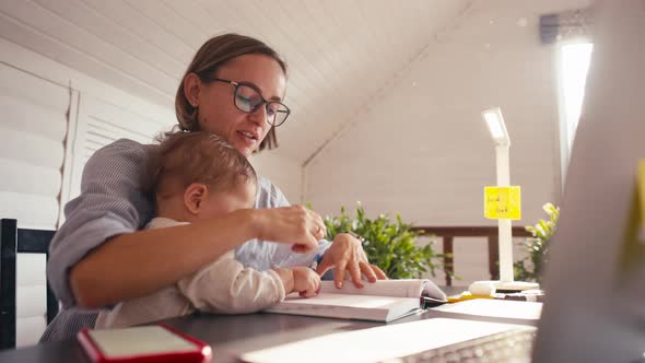 A Young Mother is Working at Home Using Computer While She's Taking Care of Her Baby alt