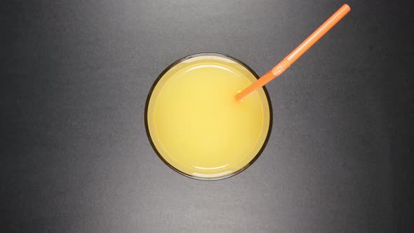 Human hand puts a tube to a glass with an orange juice (top view)
