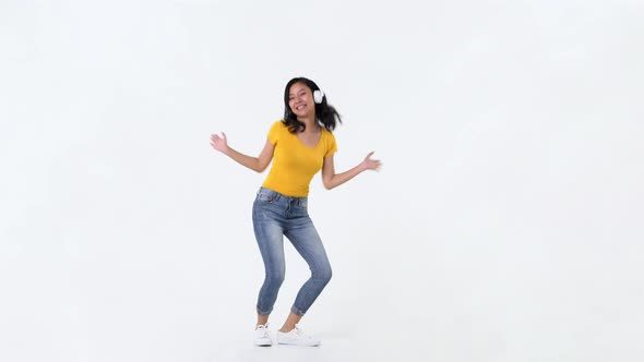 Young happy smiling Asian woman with headphones listening to music and dancing