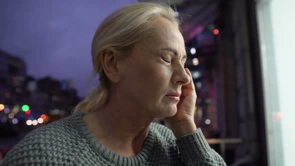 Exhausted Woman Massaging Temple and Breezing Fresh Air on Apartment Balcony