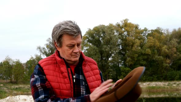 Mature Adult Man in Cowboy Hat and Cowboy Clothes Brushes His Hat, Shake Off Dust. alt
