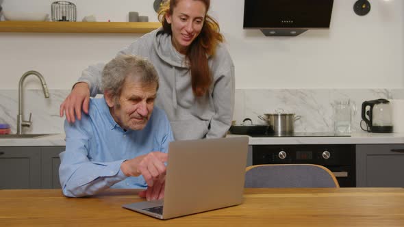 Happy Grandfather and Daughter Hugging Looking at Something on a Laptop at Home alt