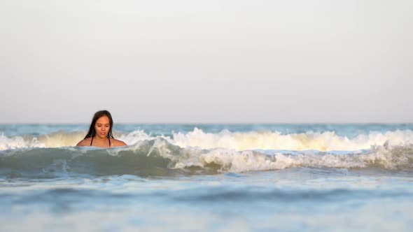 Girl with Wet Hair in a Leopard Swimsuit Splashes Water While Sitting in the Sea alt