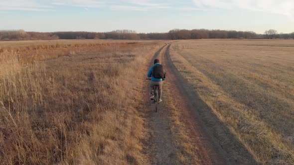 Aerial View of a Cyclist Riding on His Bicycle in Mountain at Sunset. alt