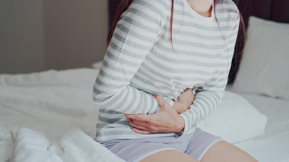 Young woman having stomach ache on the bed. Periods cramp problems concept