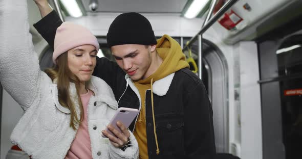 Millennial Smiling Couple Looking at Phone Screen While Watching Videoclip. Young Guy and His alt