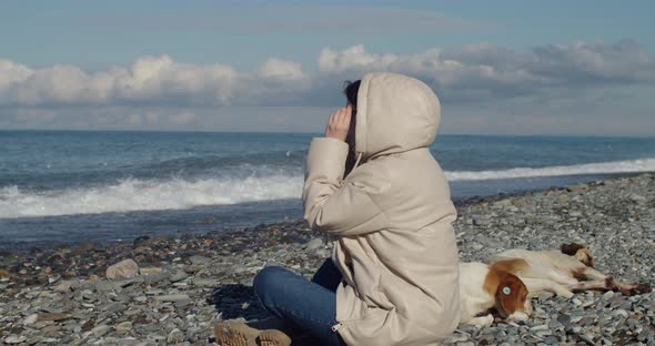 Young Woman Sitting on Seashore with Dogs and Enjoying the Sea View