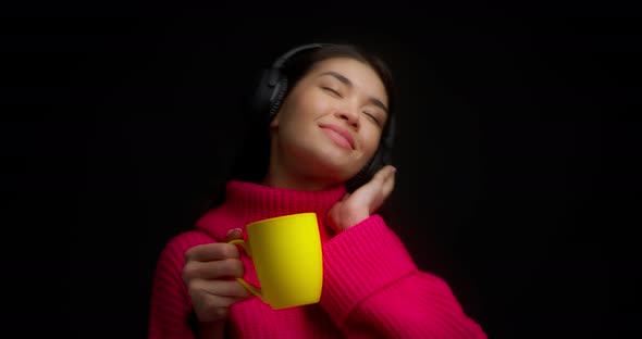 Cute Woman Enjoy Music with Wireless Headphones and Drinks From a Yellow Mug
