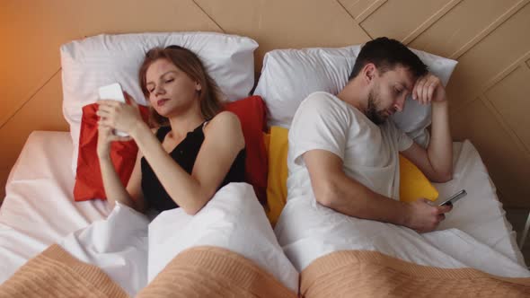 Couple using smartphones on a date. The concept of phone addiction. Couple is lying in bed backs alt