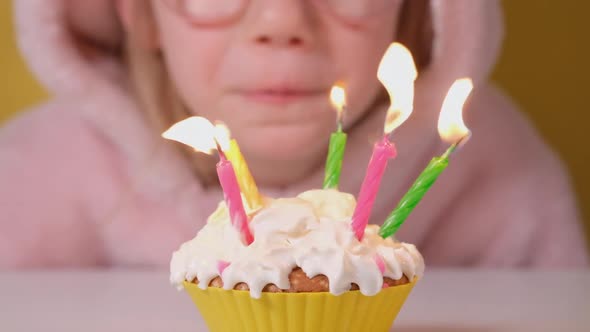 Happy Child Girl in Pink Overalls Blowing Out Five Candles on Birthday Cake at Party alt