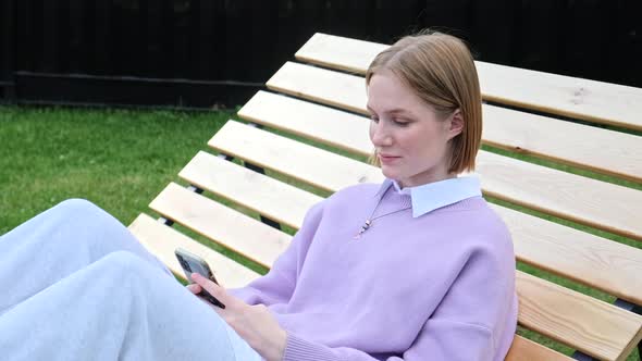 Short Haired Young Woman in Pullover Types on Smartphone alt