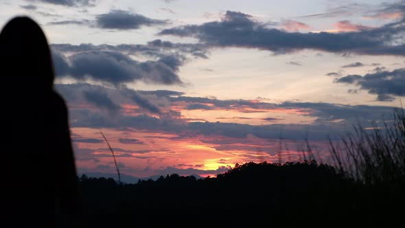 Silhouette of a female walking and watching sunset sky on the mountain peak