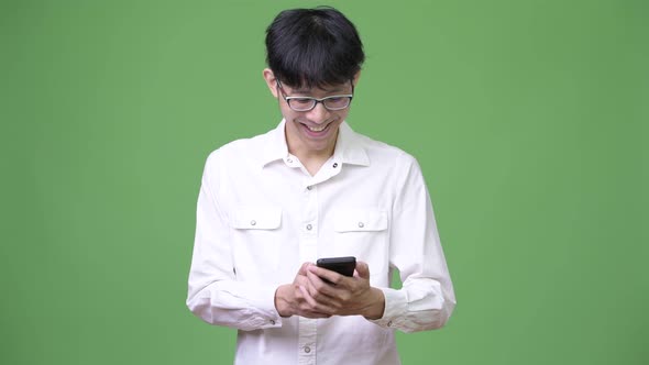 Happy Young Asian Businessman Smiling While Using Phone alt