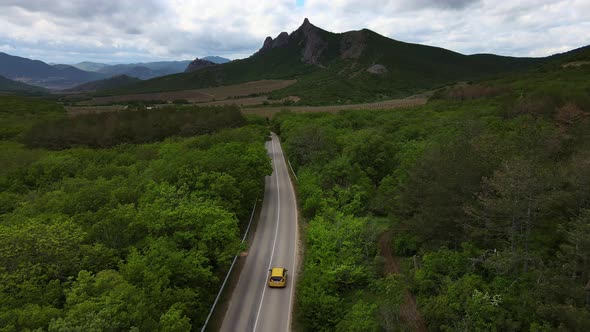 A Car Drives Down a Paved Road in a Mountainous Area That Cuts Through a Forest alt