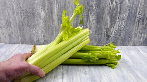 Person puts a bunch of fresh celery on a gray wooden table