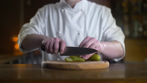The Cook Cuts Pickle on the Wooden Board in a Bar in Slow Motion, Cooking Burger and Salad alt