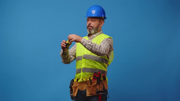 Senior Man Builder Using Measuring Tape Against Blue Background