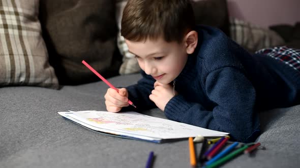 handsome little boy draws with colored pencils in coloring book lying down. Creativity