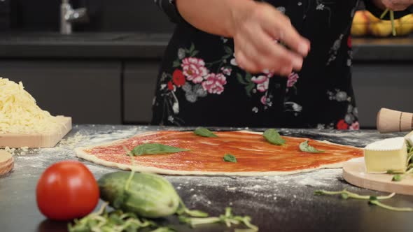 Female adding basil leaves to italian pizza margherita. alt
