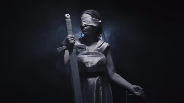 Greek Goddess Themis Blindfolded Holds Sword and Raise Scales Turning Head on Black Background with alt