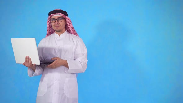 Arab Man on an Isolated Blue Background with Laptop Looking at Camera alt