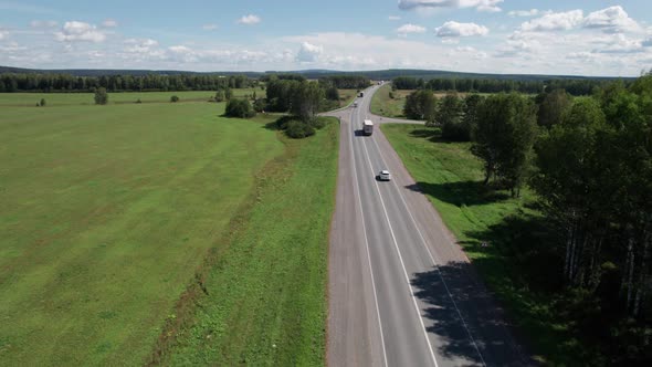Aerial View of Scenic Road Between Green Trees with Pines on a Sunny Summer Morning alt