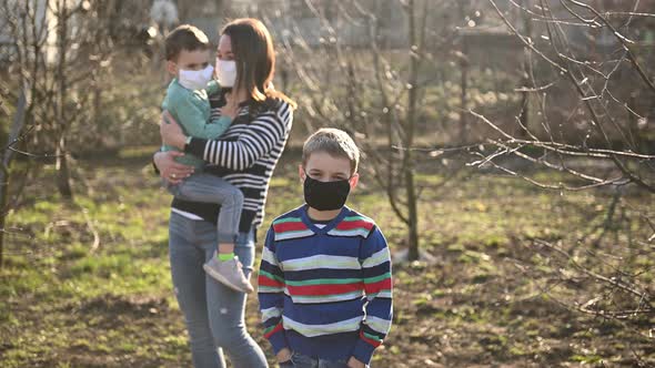 Caring Mother Hugs the Masked Child, and the Second Child Is in Front