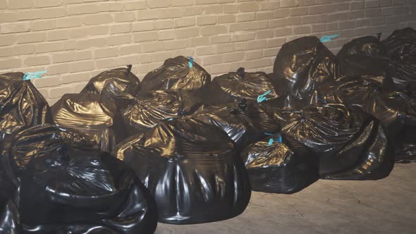 An endless pile of black plastic garbage bags against dirty brick wall loop. 4K