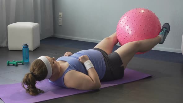 Obese Girl Trying to Train Lower Body Muscles Raising Big Gym Ball With Her Legs alt