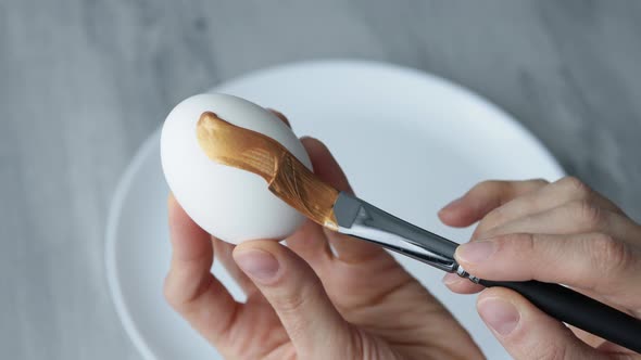 Close-up. Female hands paint Easter egg in a modern minimalist style with colorful paint.