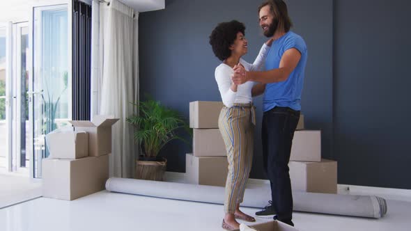 Mixed race couple dancing together in between cardboard boxes at new apartment house alt
