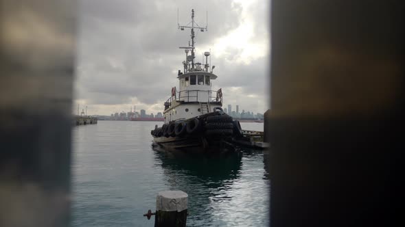Push in of tug boat docked at pier through waterfront railing. alt