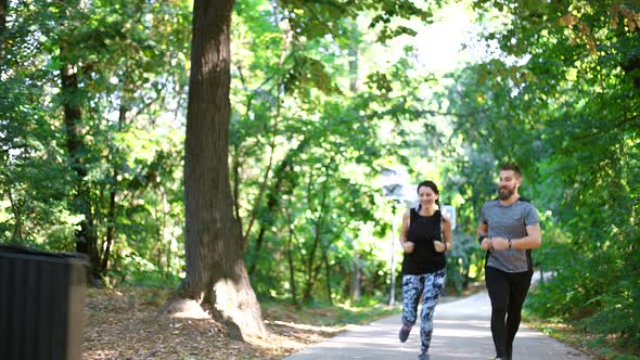 Sporty couple running on forest path, man looking on smartwatch