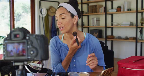 Mixed race female vlogger applying make up and recording on digital camera at home alt