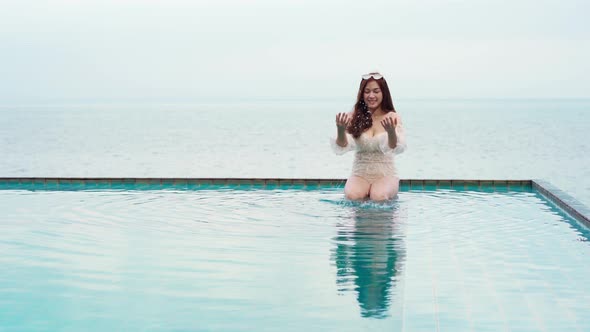 young woman playing water splash in swimming pool with sea background alt