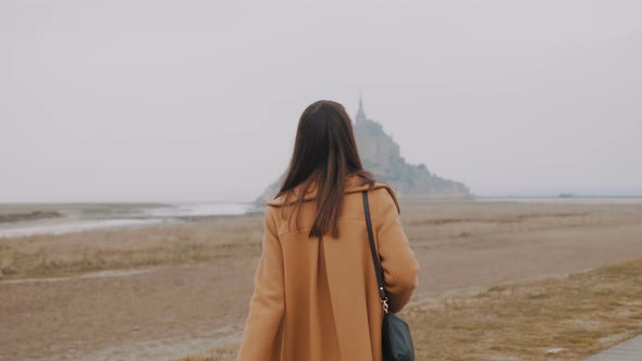 Beautiful Brunette Blogger Woman Smiling at Camera, Taking Picture of Epic Foggy Mont Saint Michel alt