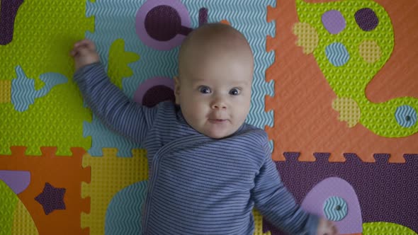 Joyful Newborn with Outstretched Arms Lying on Carpet and Looking at Camera alt
