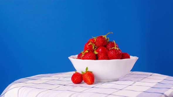 A Plate with Ripe Strawberries Rotates on a Blue Background