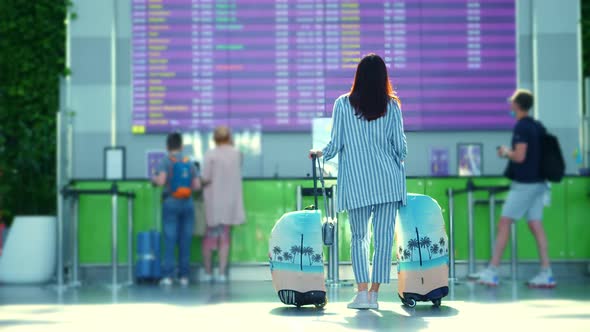 Air Passenger, Female Tourist, with Luggage, Standing Against Departure Board at Airport alt