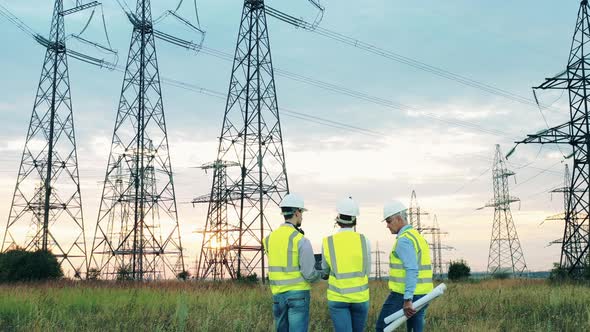 Power Engineers Are Walking Along the Field with Electrical Towers alt