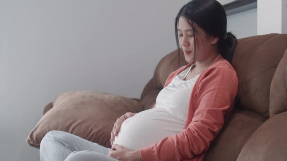 Young Asian Pregnant woman holding her belly talking with her child feeling happy smiling.
