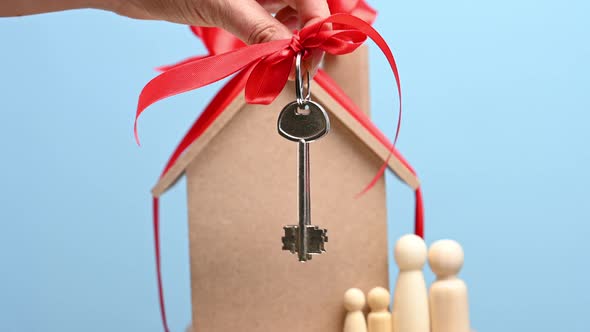 female hand holds a metal key with a red ribbon on the background of a model house alt