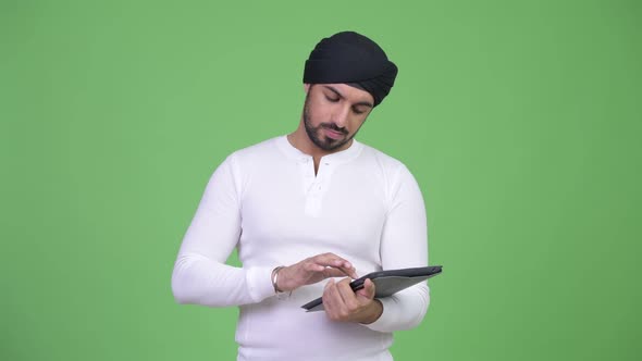 Young Handsome Bearded Indian Man Thinking While Using Digital Tablet