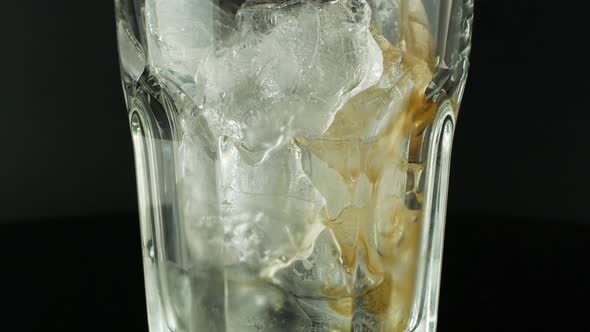 Pouring cola with ice cubes close-up. Cola with Ice and bubbles in glass on a black background. alt