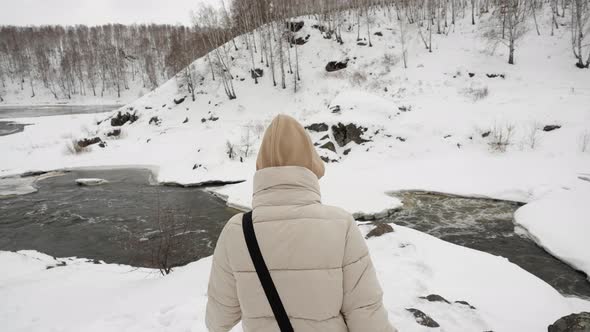 A Girl Tourist in a Hood and with Red Hair Walks on the Snowy Mountains