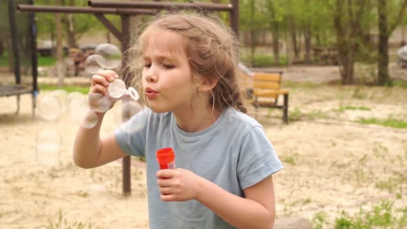 A Little Shaggy Girl in a Blue Tshirt Inflates Soap Bubbles in the Park alt