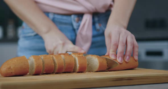 Woman Skillfully Cutting Homemade Bread on Cutting Board on Kitchen Table alt