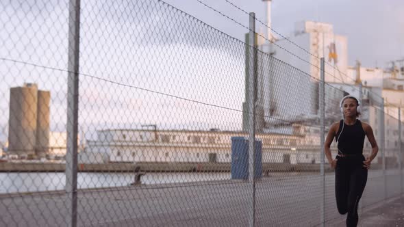 Young Woman In Sportswear And Headphones Running Along Harbour alt