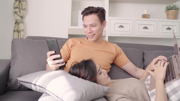 Asian couple using smartphone and laptop checking social media in living room. alt